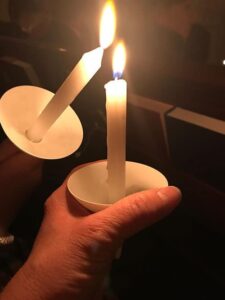 Two lit candles held in hands during a vigil.