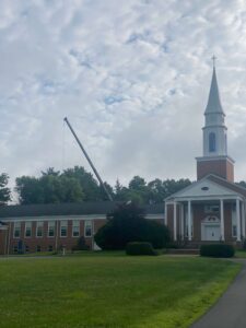 Church with a tall spire and crane in the background under a cloudy sky.