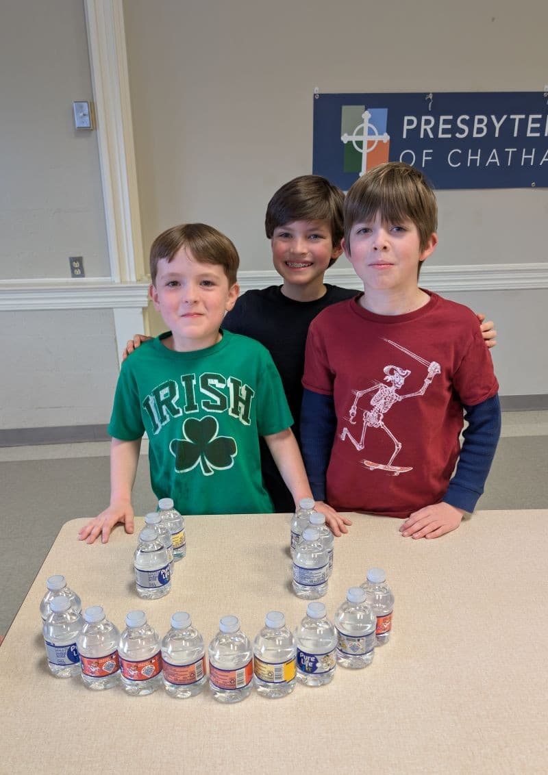 Three boys standing behind a table with water bottles.