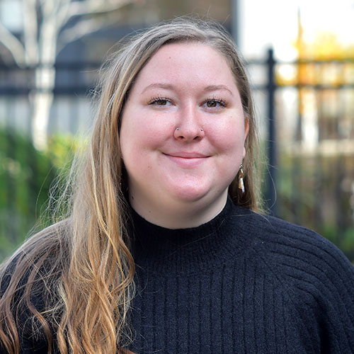 Smiling woman with long hair in a black sweater outdoors.