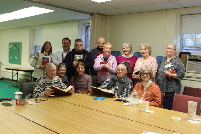 Group of elderly people and a few younger adults gathered around a table, smiling.