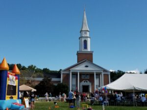 A church with a steeple and people gathered outside during a sunny day.