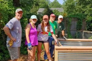 Group of six people outdoors assembling a wooden structure on a sunny day.