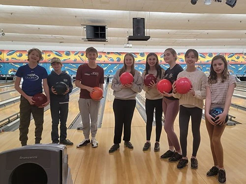 A group of children holding bowling balls at a bowling alley.