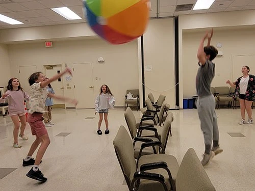 Three people playing with a colorful beach ball indoors.