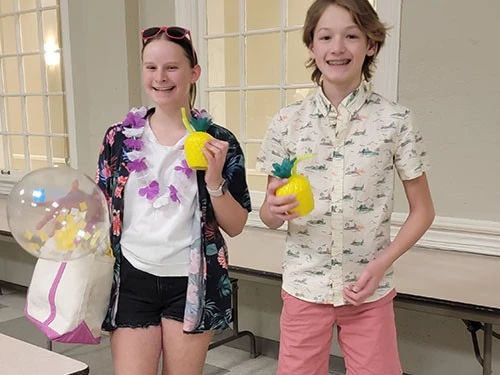 Two kids smiling, holding colorful drinks with straws.