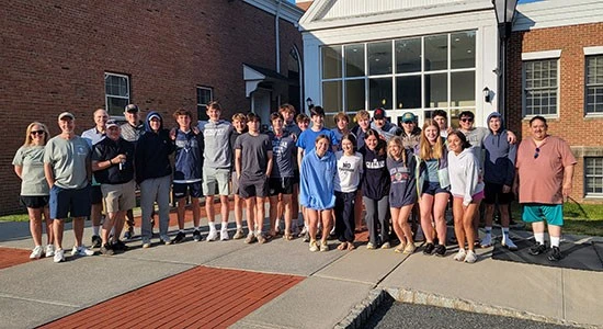Group of students posing outside a school building on a sunny day.