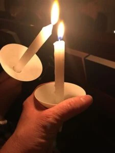 Two lit candles held in hands during a vigil.
