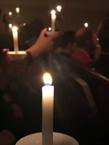 A single candle flame glowing amid a crowd holding candles.