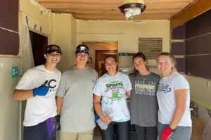 Five friends posing together indoors, smiling and relaxed.