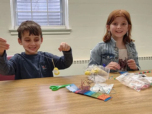 Two children happily crafting at a table with art supplies.
