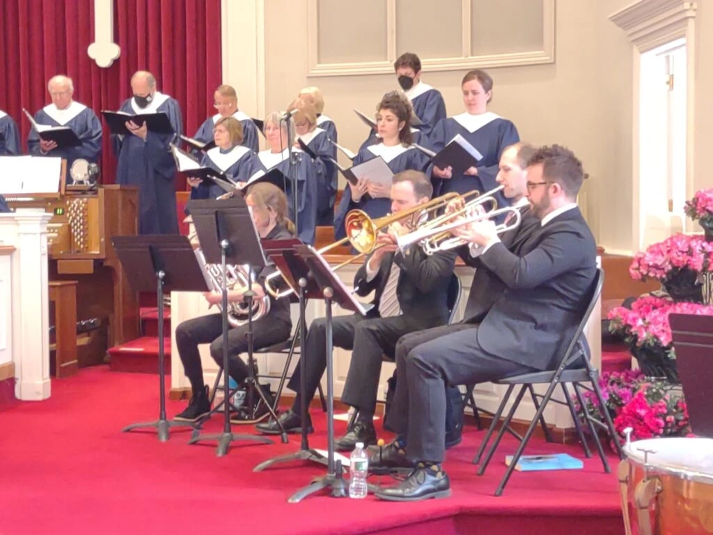 A choir and brass band perform together in a church.