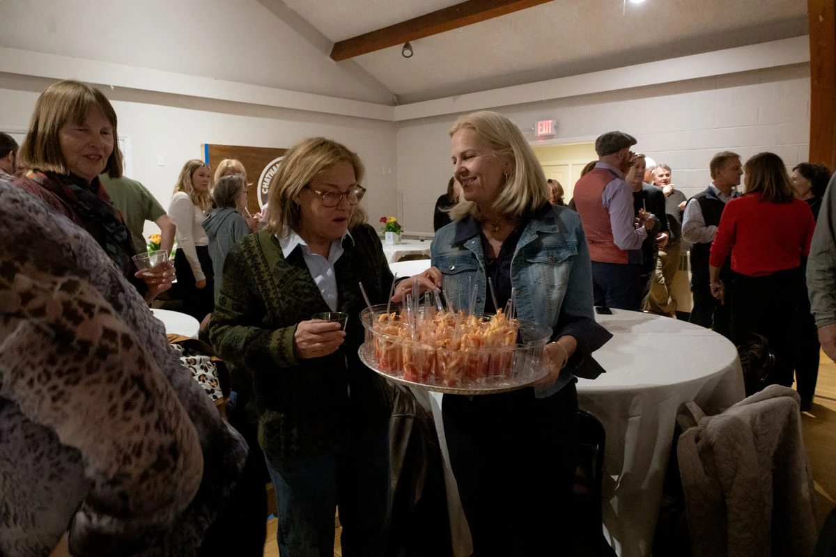 Two women share appetizers at a lively indoor gathering.