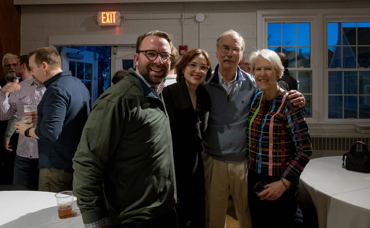 Four people smiling together indoors, casual setting with warm lighting.