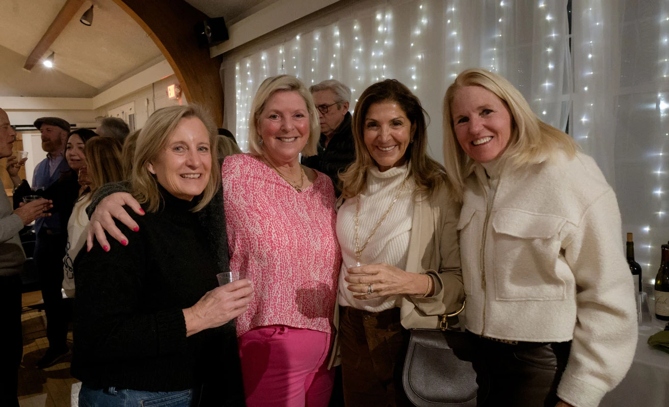 Four women smiling and posing together at a festive indoor gathering.