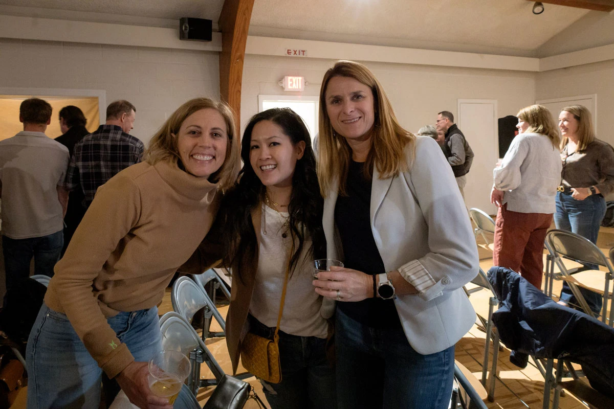 Three women smiling and posing indoors at a social event.