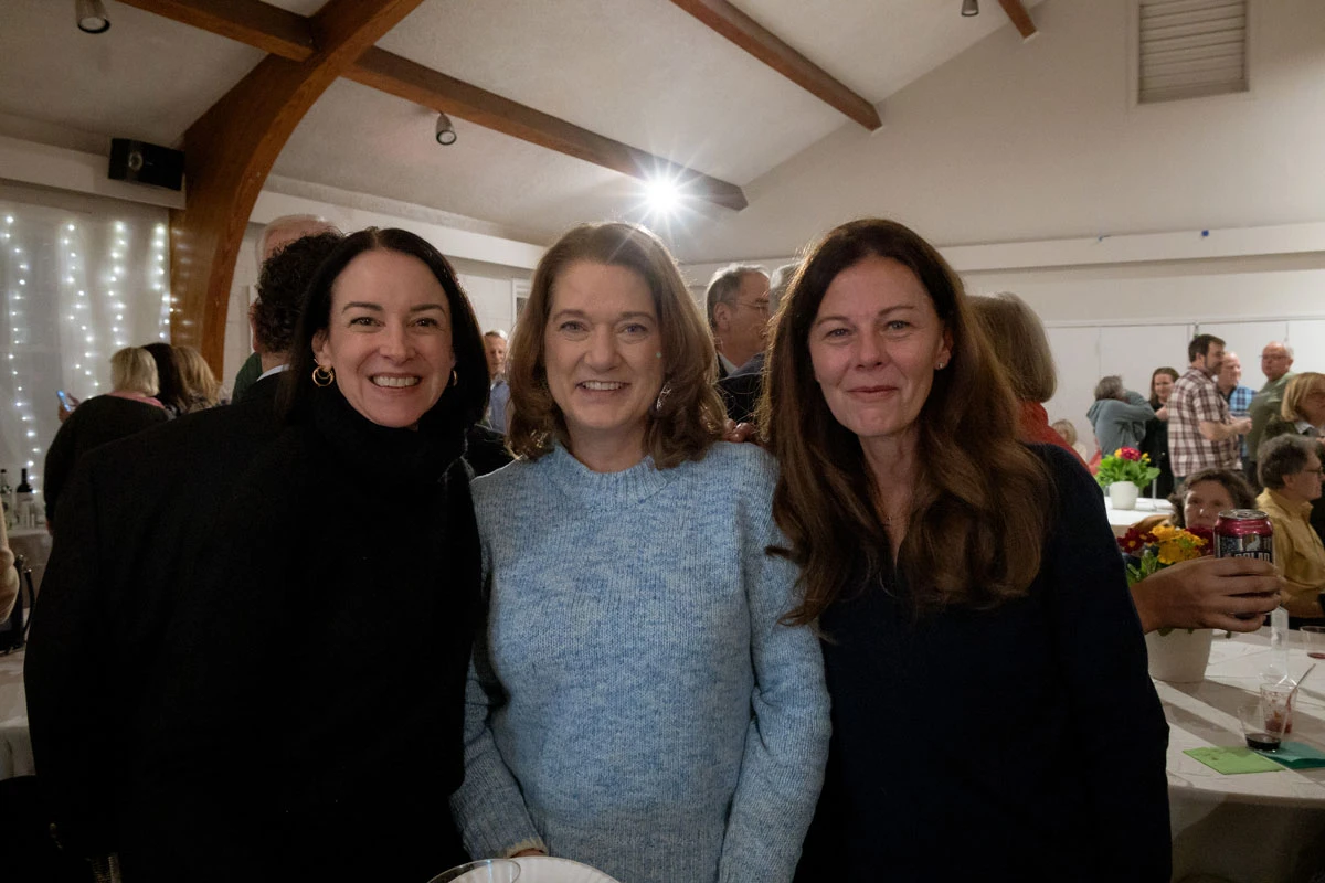 Three women smiling indoors under wooden beams.