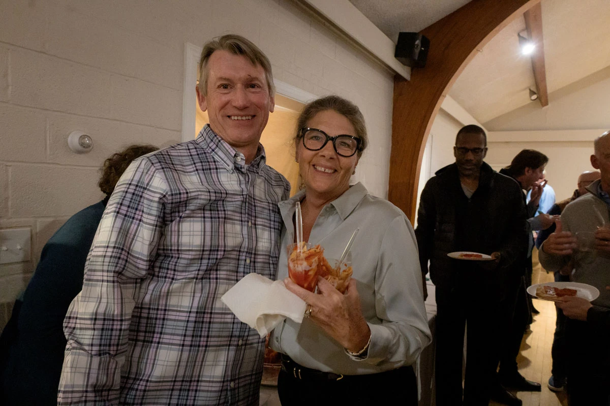 Two people smiling and posing indoors, one holding a drink and a napkin.