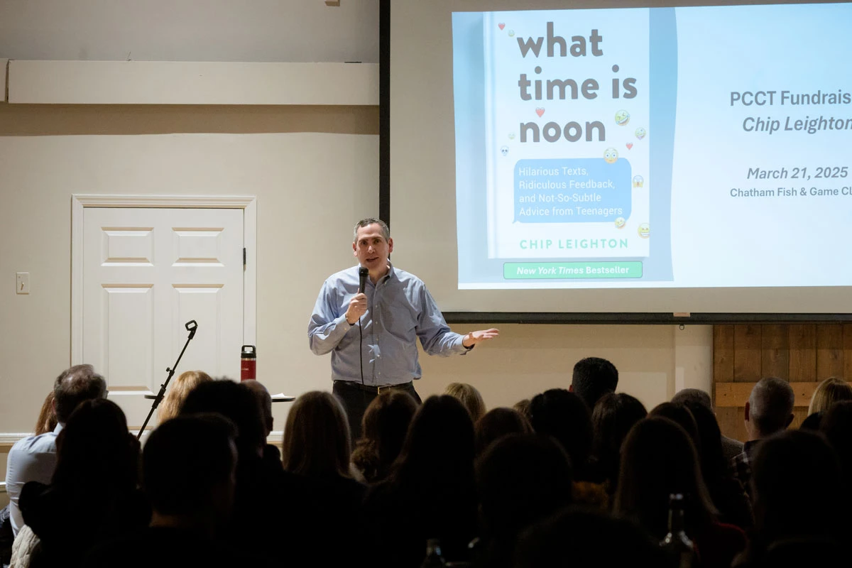 A man speaks to an audience with a slide titled 'what time is noon' behind him.