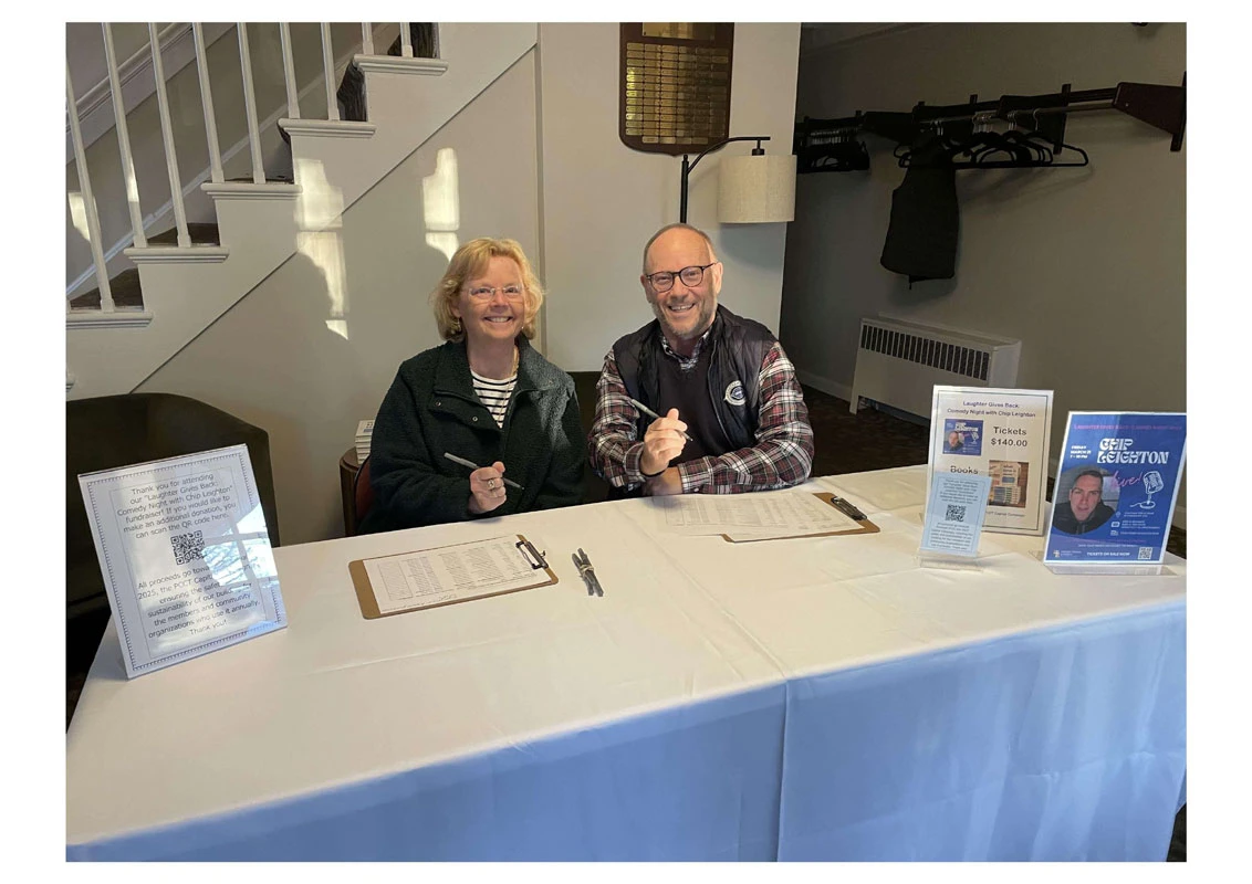 Two people sitting at a table smiling with papers and pens.