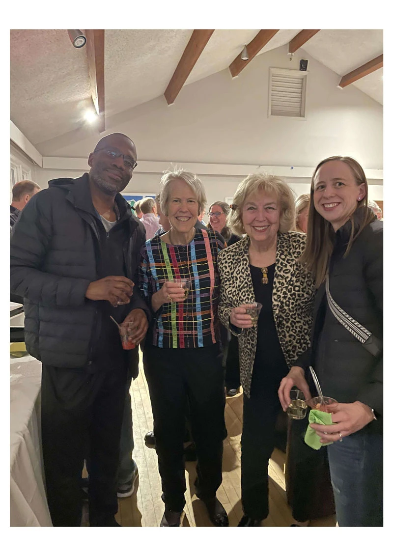 Four adults smiling and posing together indoors at a social event.