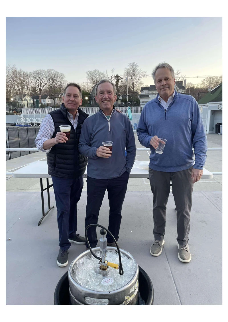 Three men holding drinks, standing outdoors near a keg.