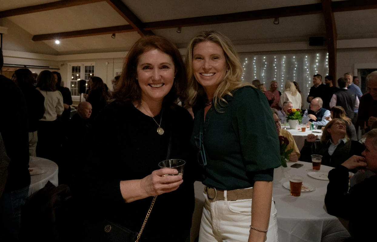 Two women smiling at a social event, one holding a drink.