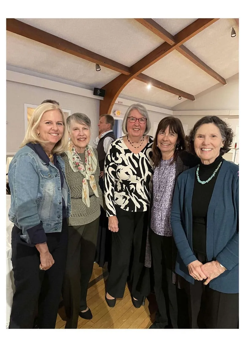 Five women standing together indoors, smiling at the camera.