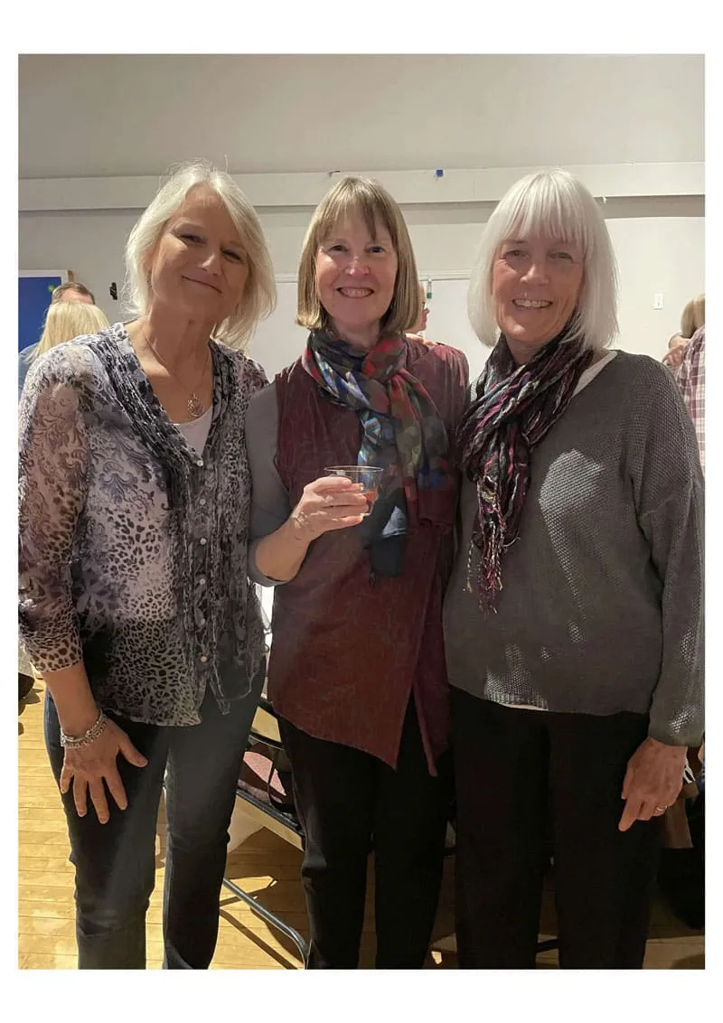 Three women standing indoors, smiling and posing together.
