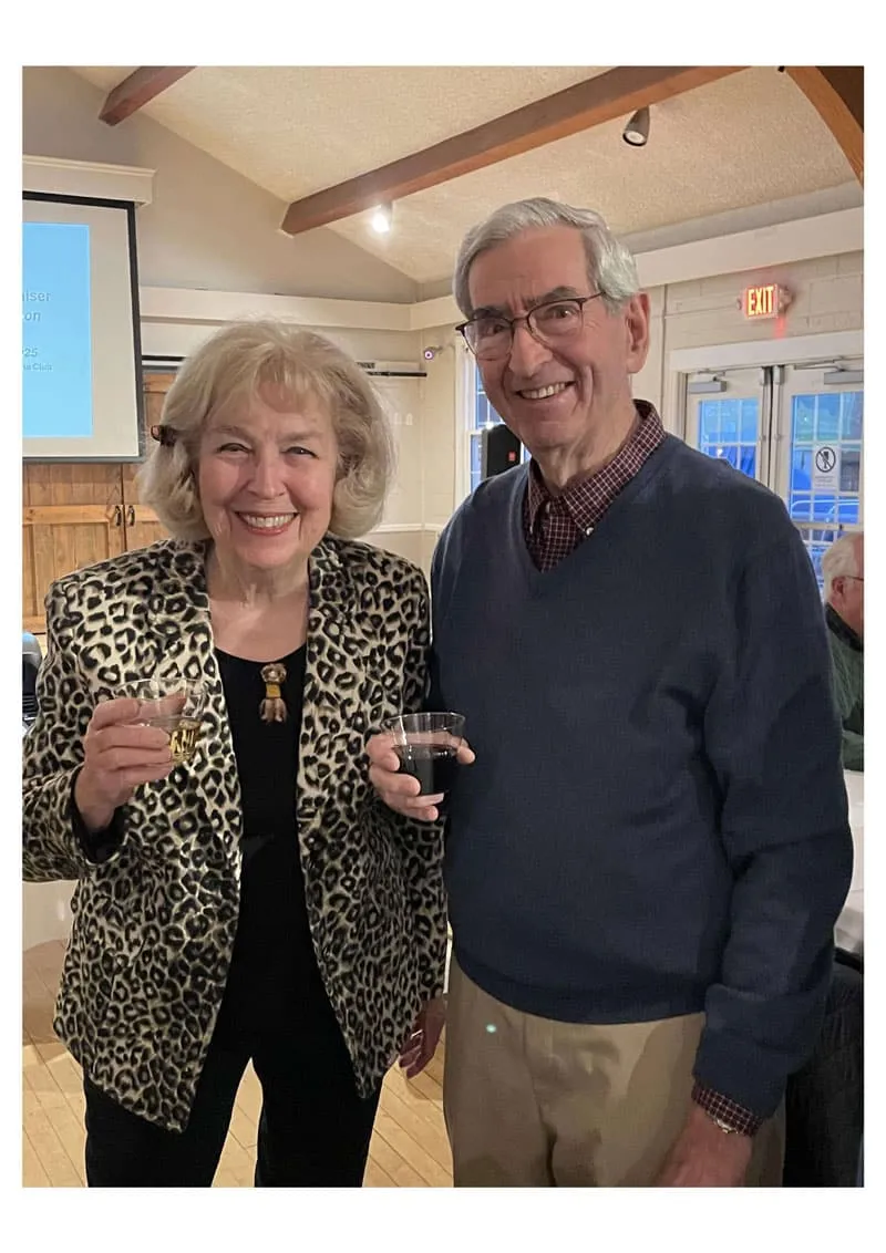 Elderly couple smiling with drinks in hand at a social gathering.
