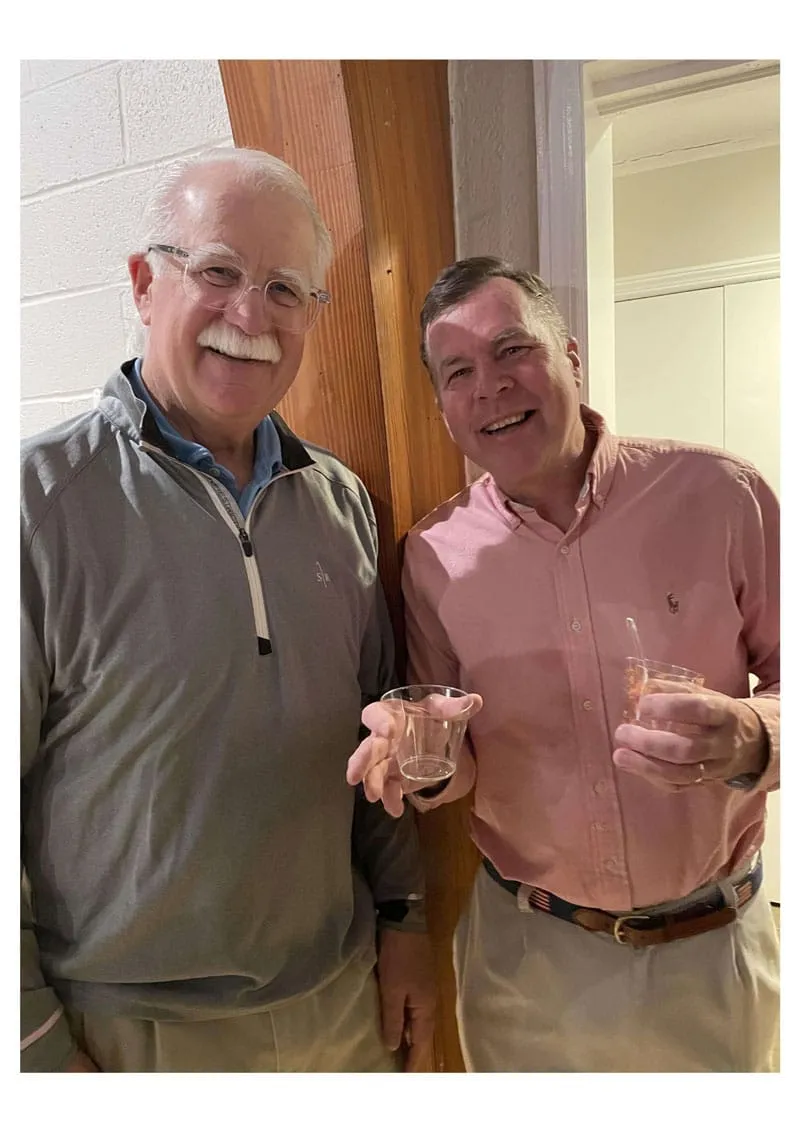 Two smiling men holding drinks, standing indoors.