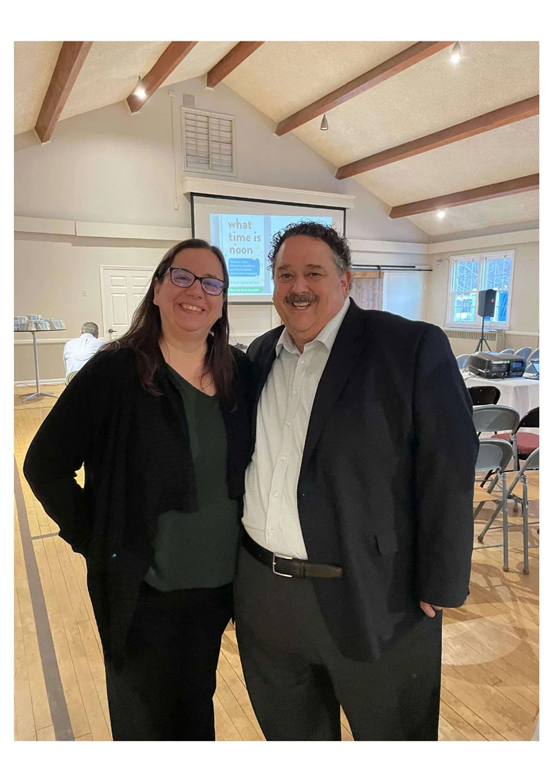 Two people posing indoors in business casual attire, smiling.