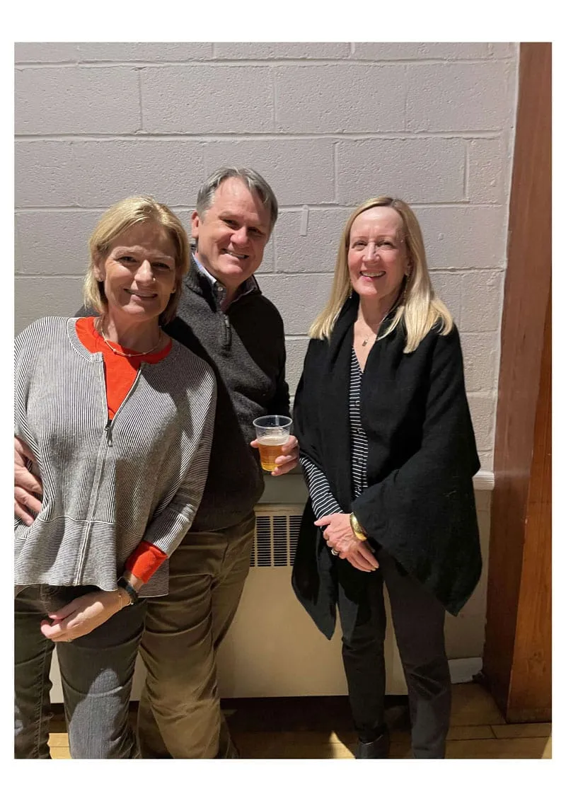 Three people posing together by a wall, smiling warmly.
