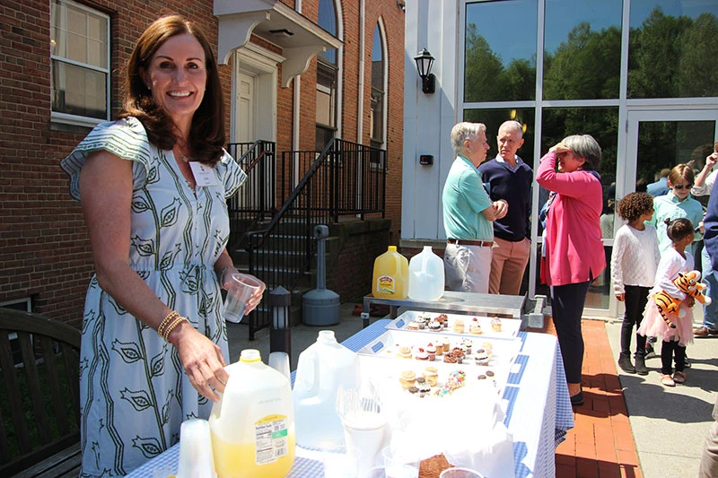 Woman serving food and drinks at an outdoor event on a sunny day.