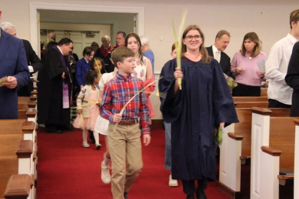Woman and boy walking down church aisle holding palm branches.