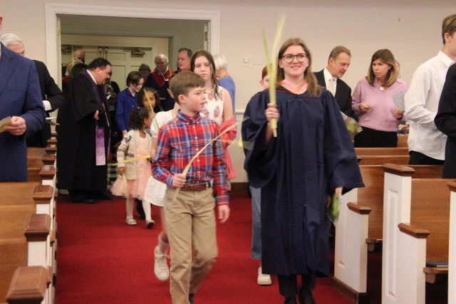 Woman and boy walking down church aisle holding palm branches.