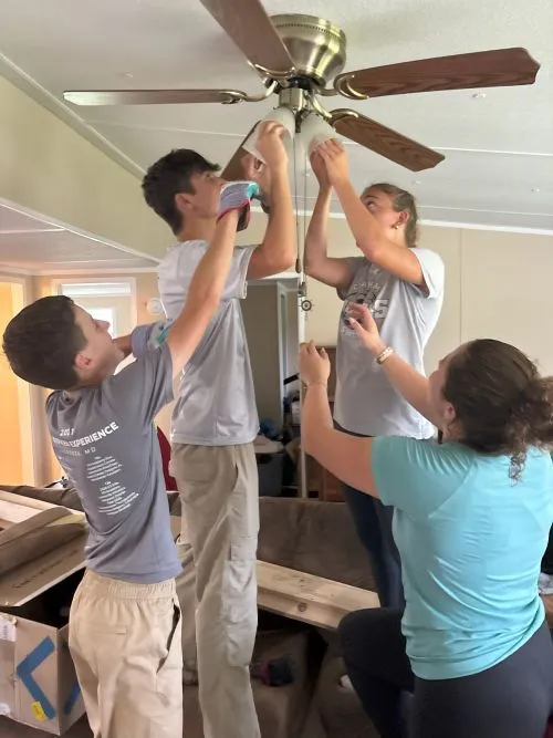 Four people working together to install a ceiling fan indoors.