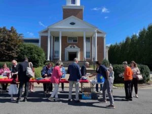 People gathered outdoors near a brick building with columns and a bell tower.